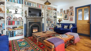 A cozy living room with a fireplace, bookshelves, a blue sofa, and a patterned rug. - Church Garden Apartment (Malvern)