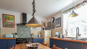 A kitchen with a wooden table, blue cabinets, a vintage stove, and decorative tiles. - Church Garden Apartment (Malvern)