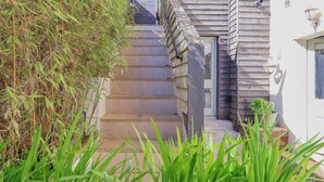 A staircase leading to a door, surrounded by greenery and a white building with wooden siding. - Church Garden Apartment (Malvern)