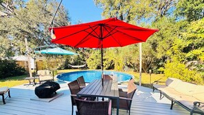 Eine Terrasse mit Pool, Gartenmöbeln und Sonnenschirmen.