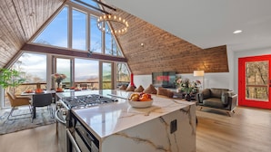 A modern kitchen with a large island, a dining area with a view, and a cozy living space with a red door.