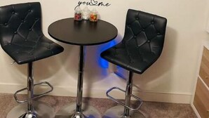 Un petit coin repas avec deux chaises en cuir noir, une table ronde et un tableau représentant des fleurs blanches, accroché au mur.