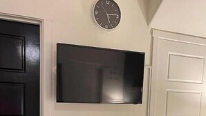 Un téléviseur fixé au mur, au-dessus d’une cheminée, avec une horloge placée au-dessus.