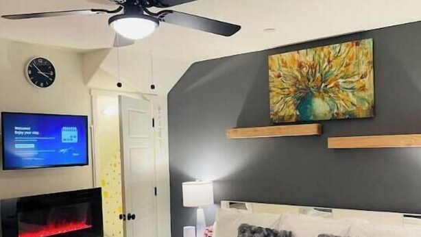 Une chambre à coucher avec un lit, un ventilateur de plafond, une télévision, une cheminée et un tableau au mur.