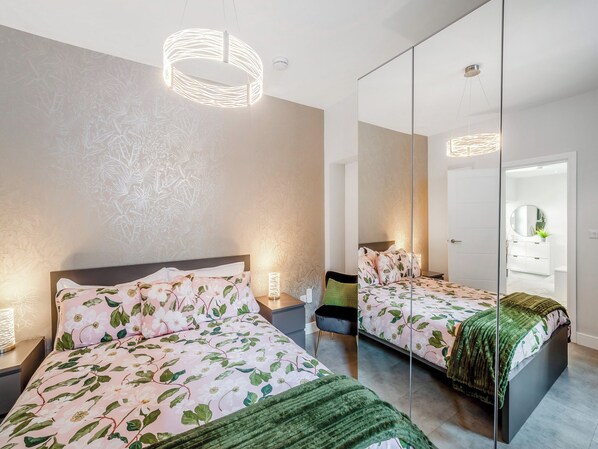 A modern bedroom with a large mirror, floral bedding, and a unique light fixture.