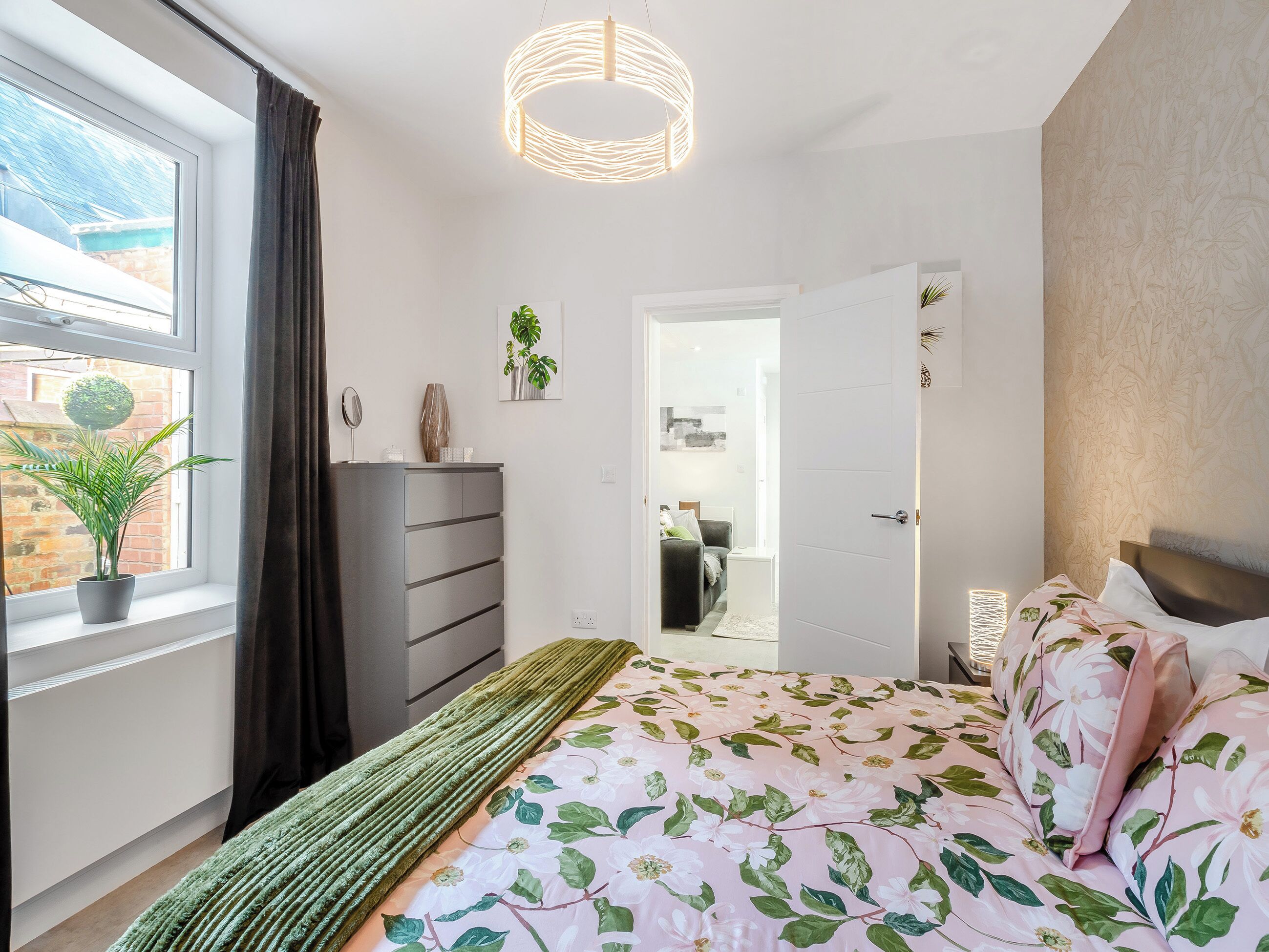A bedroom with a bed, dresser, and a potted plant by the window.