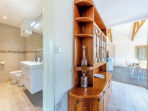 A modern bathroom with a white sink, a mirror, and a toilet. There is a wooden cabinet with glassware and a plate on top.