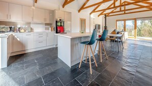 A modern kitchen with white cabinets, a central island, and blue bar stools. - 1 bedroom accommodation in Llandeilo (Llandeilo)