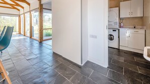 A modern kitchen with a built-in washer and dryer, a dining area with a blue chair, and a large window providing natural light. - 1 bedroom accommodation in Llandeilo (Llandeilo)