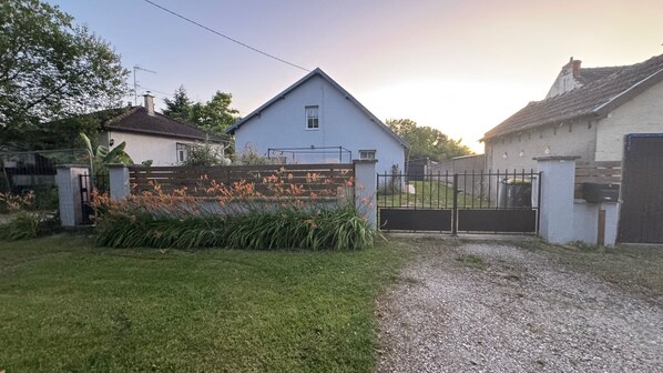 Il s’agit d’une propriété résidentielle dotée d’une entrée sécurisée par un portail, d’une pelouse agrémentée de plantes à fleurs et d’une maison à la façade bleue.