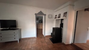 Een kamer met een televisie op een dressoir, een deur die naar een andere kamer leidt, en een plank met ingelijste foto's.
