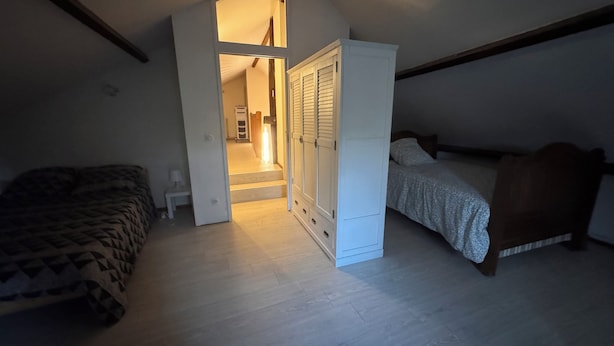 Een slaapkamer met een bed, een kledingkast en een trap naar een aangrenzende kamer.
