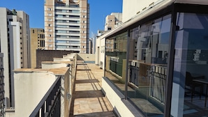 A rooftop corridor with a glass balustrade, a metal railing, and a view of high-rise buildings in the background.