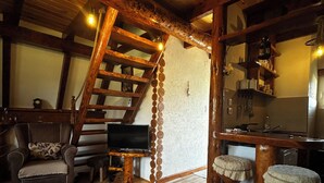 Un interior acogedor de cabaña con una escalera de madera, un televisor, un sofá y una zona de cocina.