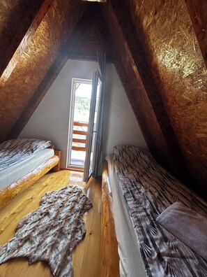 A cozy attic bedroom with wooden beams, two beds, a fur rug, and a view through a window. - Vila Sarigora - charming 2-bedroom cottage in fabulous Žabljak (Žabljak)
