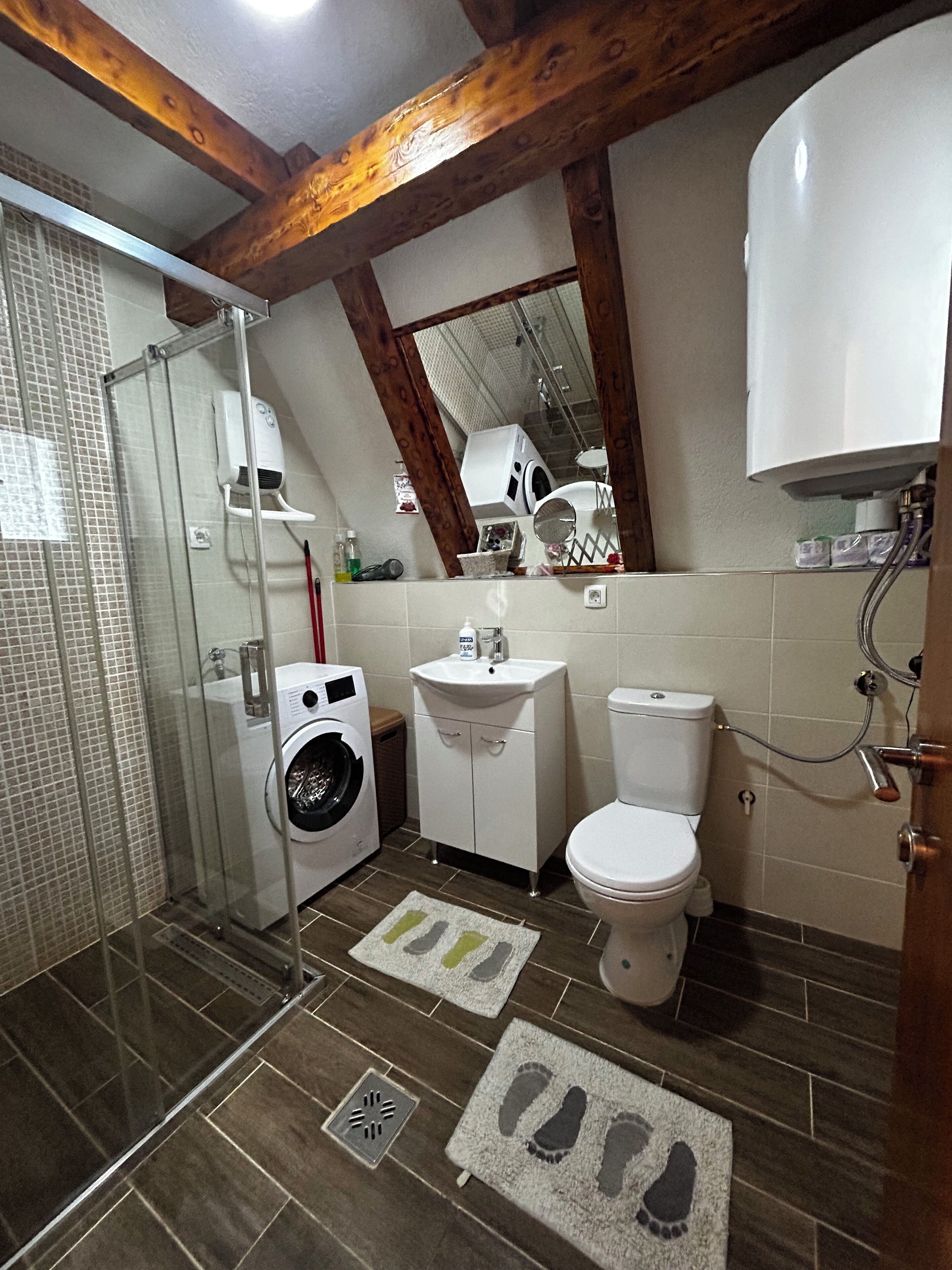 A bathroom with a glass shower enclosure, a washing machine, a sink, and a toilet.