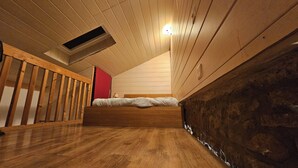 A bedroom with a sloped ceiling, wooden flooring, a bed, a red door, and a stone wall. - Apartment central near Herbstmesse & Baloise Session (Basel)