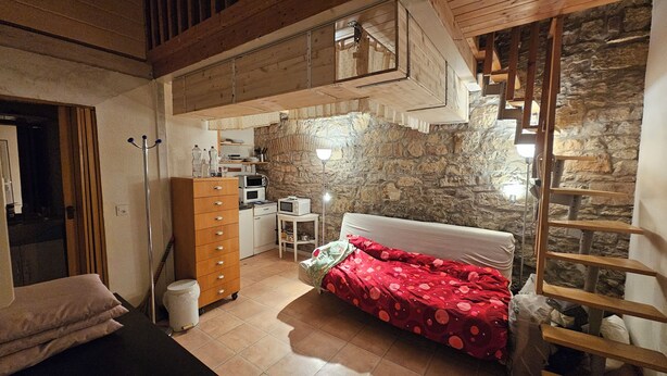A bedroom with a loft bed, a wooden wardrobe, a microwave, and a stone wall. - Apartment central near Herbstmesse & Baloise Session (Basel)