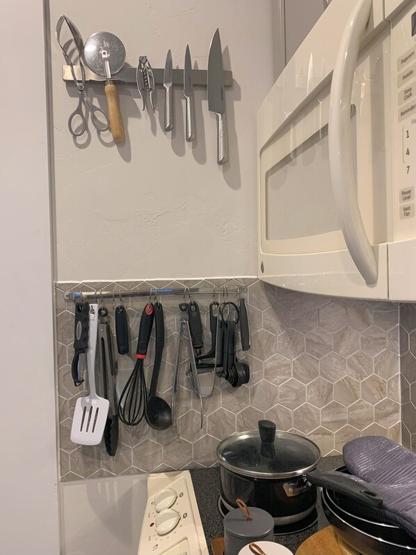 Uma cozinha com micro-ondas, uma panela no fogão e diversos utensílios pendurados em um suporte.