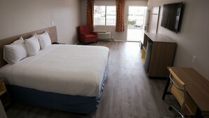 A hotel room with a large bed, a desk, a chair, a TV, and a window with curtains. - Days Inn by Wyndham Hemet (Hemet)