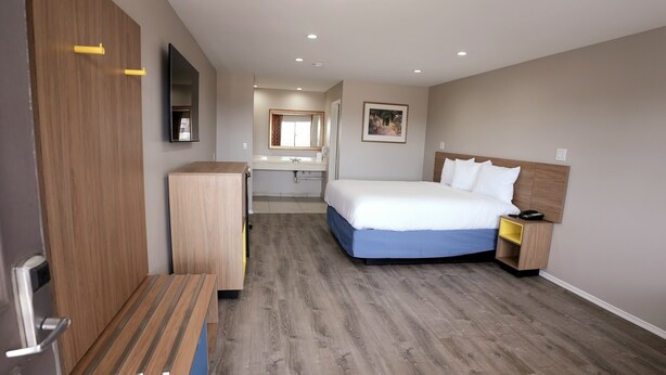 A hotel room with a bed, bedside table, wardrobe, and a mirror. - Days Inn by Wyndham Hemet (Hemet)