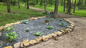 Um jardim com um caminho de cascalho, cercado por uma borda de pedra, e uma bicicleta estacionada perto.