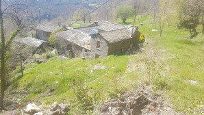 A rustic stone building with a sloped roof, surrounded by a grassy hillside and trees.