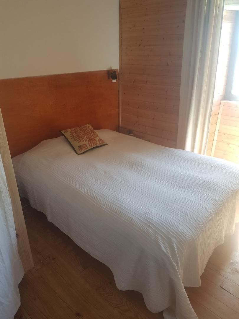A single bed with a white bedspread and a patterned pillow in a room with wooden flooring and a wooden headboard.