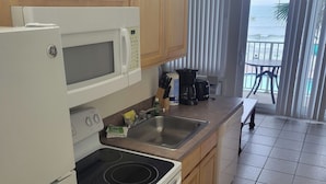 A kitchen with wooden cabinets, a microwave, a stove, and a sink. There is a view of a balcony with a table and chairs. - Gorgeous Views/Beautiful Oceanfront Condo, Beach, Pool/Hot Tub, 4th Fl, 2-Bath (Daytona Beach)