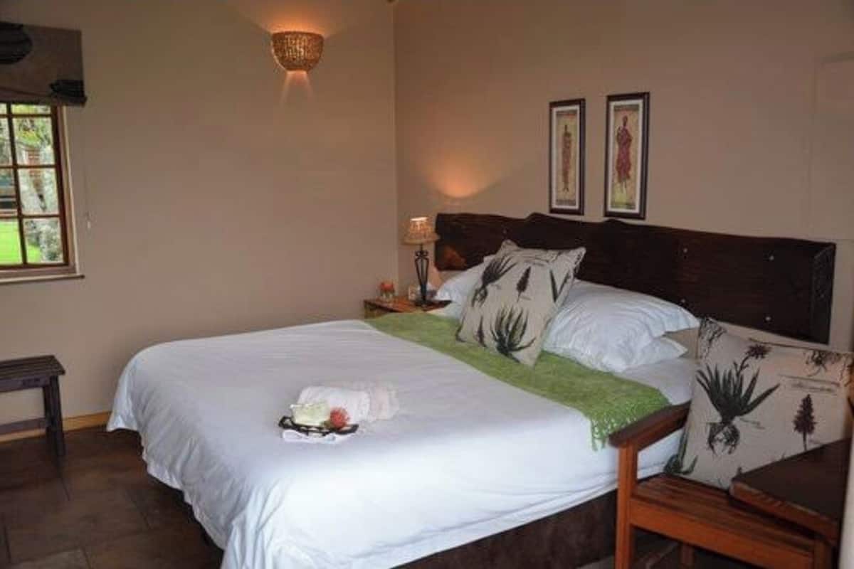 Una cama bien hecha con un plaid verde, una mesita de noche con lámpara y dos cuadros en la pared.