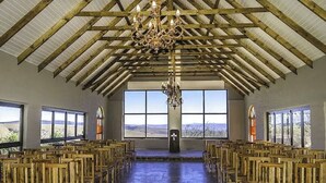 Un salón amplio con bancos de madera dispuestos en filas, un techo alto con vigas de madera y grandes ventanales que ofrecen vistas al paisaje.