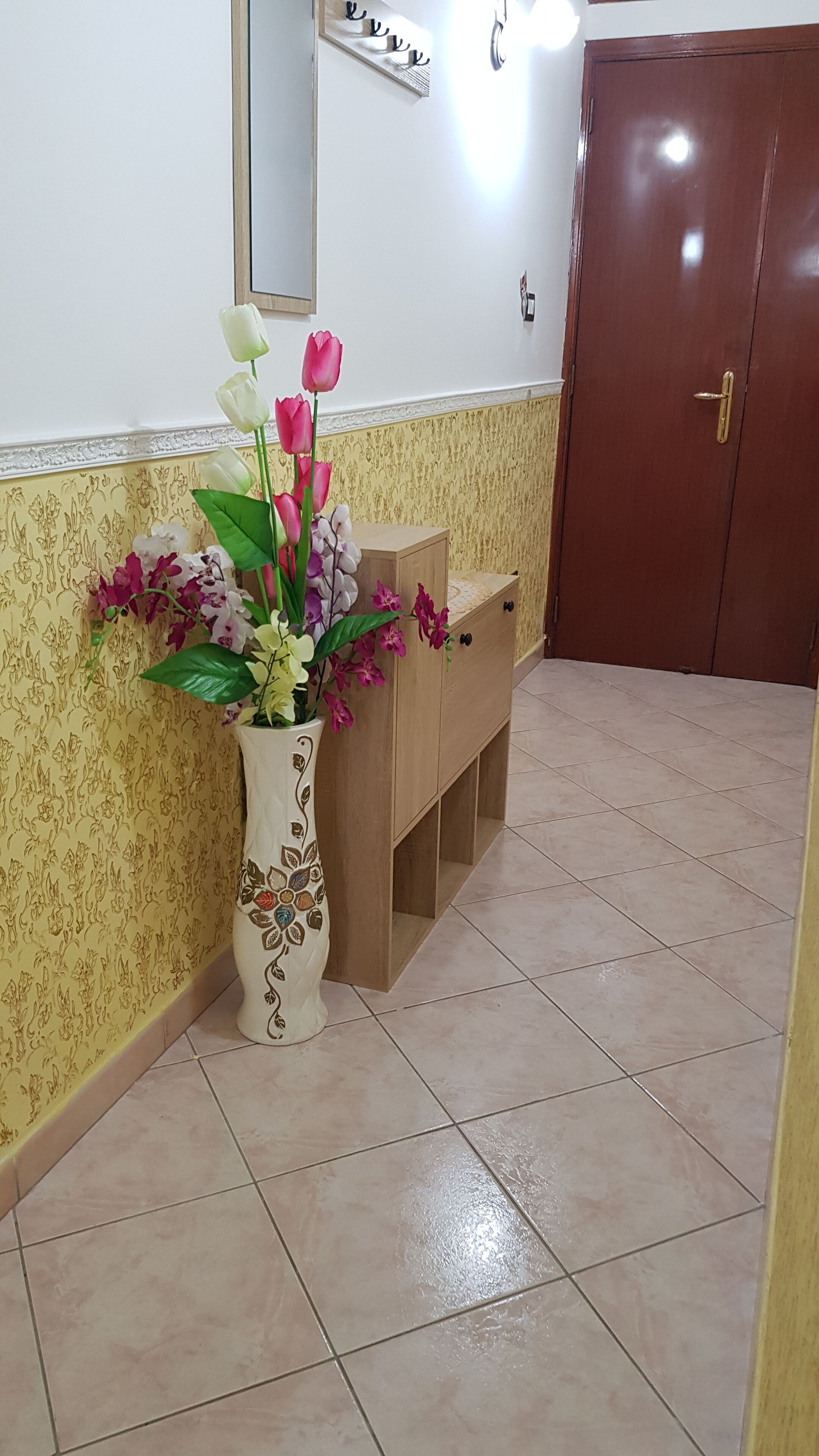 A corner with a decorative vase of flowers, a wooden cabinet, and a door.
