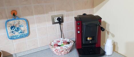 A kitchen with a coffee machine, a basket of coffee pods, and a blue floral kitchen towel on the wall.