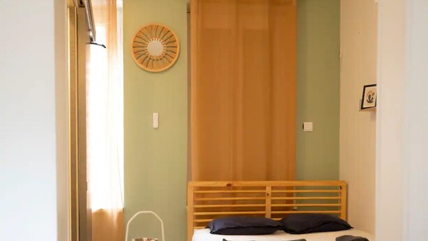 A bedroom with a wooden bed, a small chair, and a wall clock. - Cosy loft in the heart of Cambrai (Cambrai)