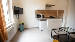 A compact kitchen with white cabinets, a microwave, a small refrigerator, and a glass-top coffee table. - Cosy loft in the heart of Cambrai (Cambrai)