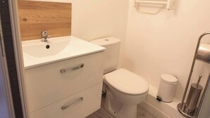 A compact bathroom with a white sink, toilet, and a small window with blinds. - Cosy loft in the heart of Cambrai (Cambrai)