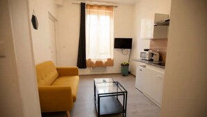 A compact living space with a sofa, a glass coffee table, a TV, and a kitchenette. - Cosy loft in the heart of Cambrai (Cambrai)