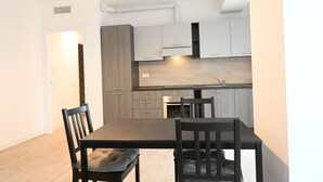 Een moderne keuken met grijze kastjes, een inbouwoven en een eethoek met een tafel en stoelen.