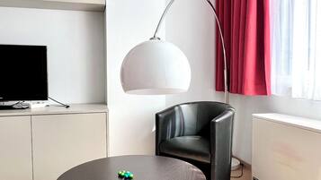 Una sala de estar moderna con una mesa redonda, un sillón de cuero negro, una lámpara de pie, un televisor de pantalla plana y un radiador.