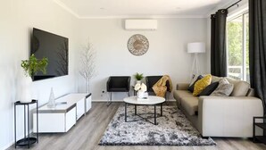 A modern living room with a sofa, coffee table, and a TV mounted on the wall. - Lake Cove Daylesford (Daylesford)