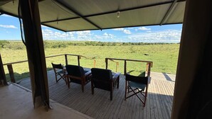Un espacio de estar techado al aire libre con sillas de madera y una mesa, con vistas a un campo cubierto de hierba.