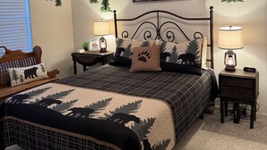 A bedroom with a bed, two bedside tables, a nightstand, a ceiling fan, an air conditioning unit, and a wall-mounted lamp.