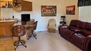 A living room with a leather couch, a TV, a wooden cabinet, and a sign that reads "Welcome to our Cabin."