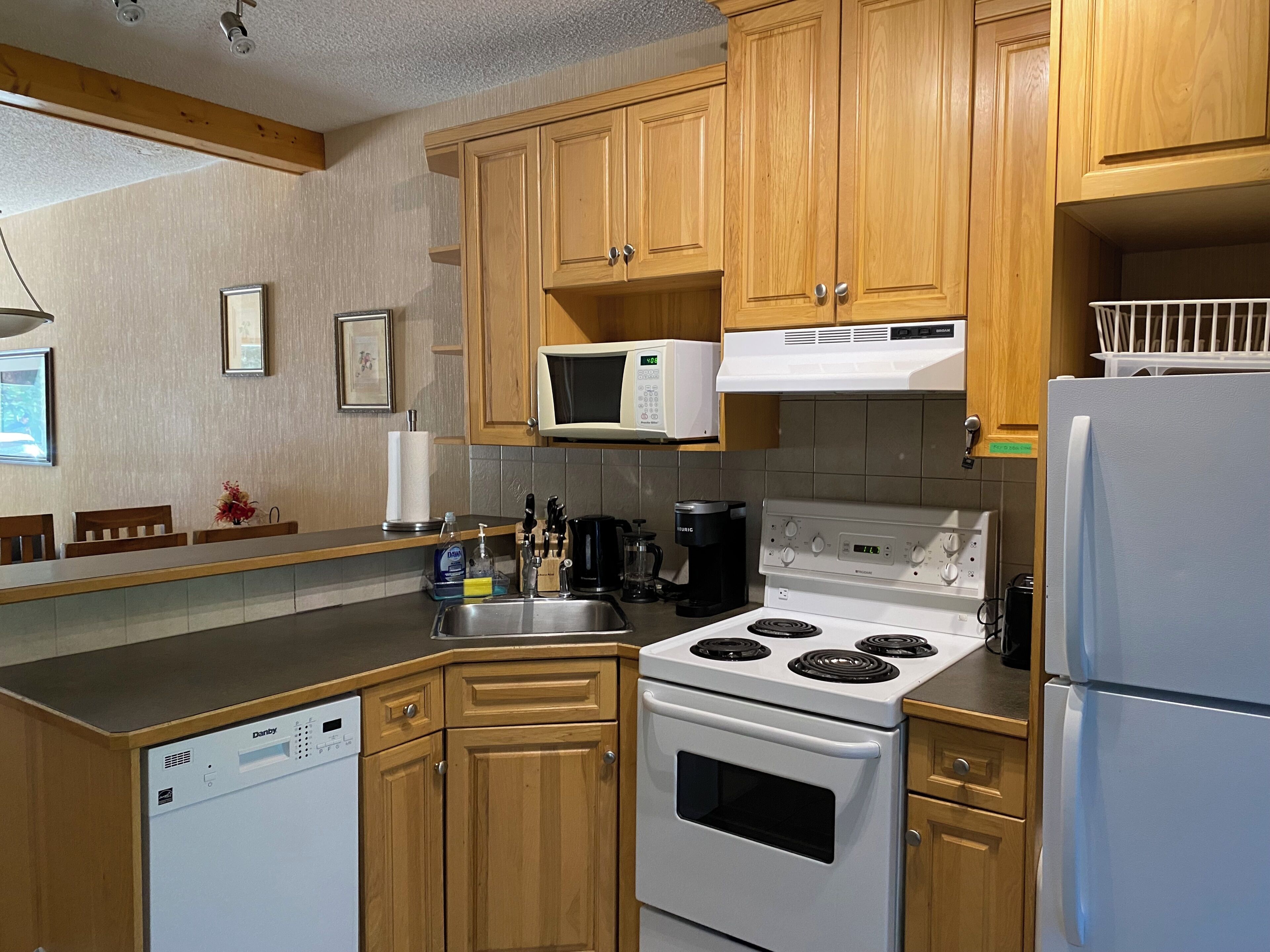 Una cocina con armarios de madera, lavavajillas, microondas, estufa y refrigerador.