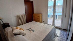 Et soveværelse med seng, kommode, radiator og en skydedør til en balkon.