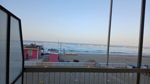 Strandudsigt fra en balkon med en bygning i forgrunden, en sandstrand og havet.