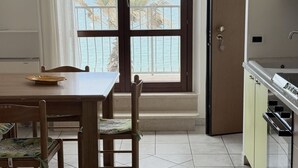 Un comedor con vista al mar, una cocina con lavamanos y una puerta que da a un balcón.