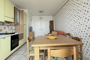 A compact kitchen with a dining area, a clock, and patterned wallpaper.
