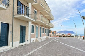 A row of multi-story buildings with balconies, a paved street, and boats in the background. - P056 – Porto Recanati, comfortable three-room apartment facing (Porto Recanati)