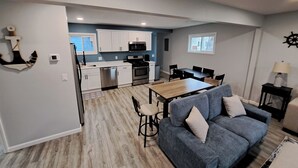 A modern kitchen with white cabinets, a dining area with a wooden table and chairs, and a blue sofa in a living room. - Beautifully remodeled house that sleeps 10 by Lake Erie Fun. (Sandusky)